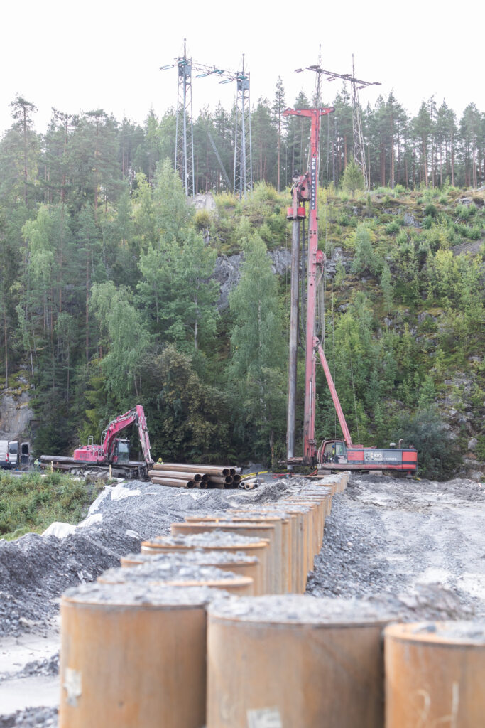 Porapaalua nostetaan poraa vasten pystysuoraan. Maahan jo asennettuja paaluja on jonossa etualalla. 